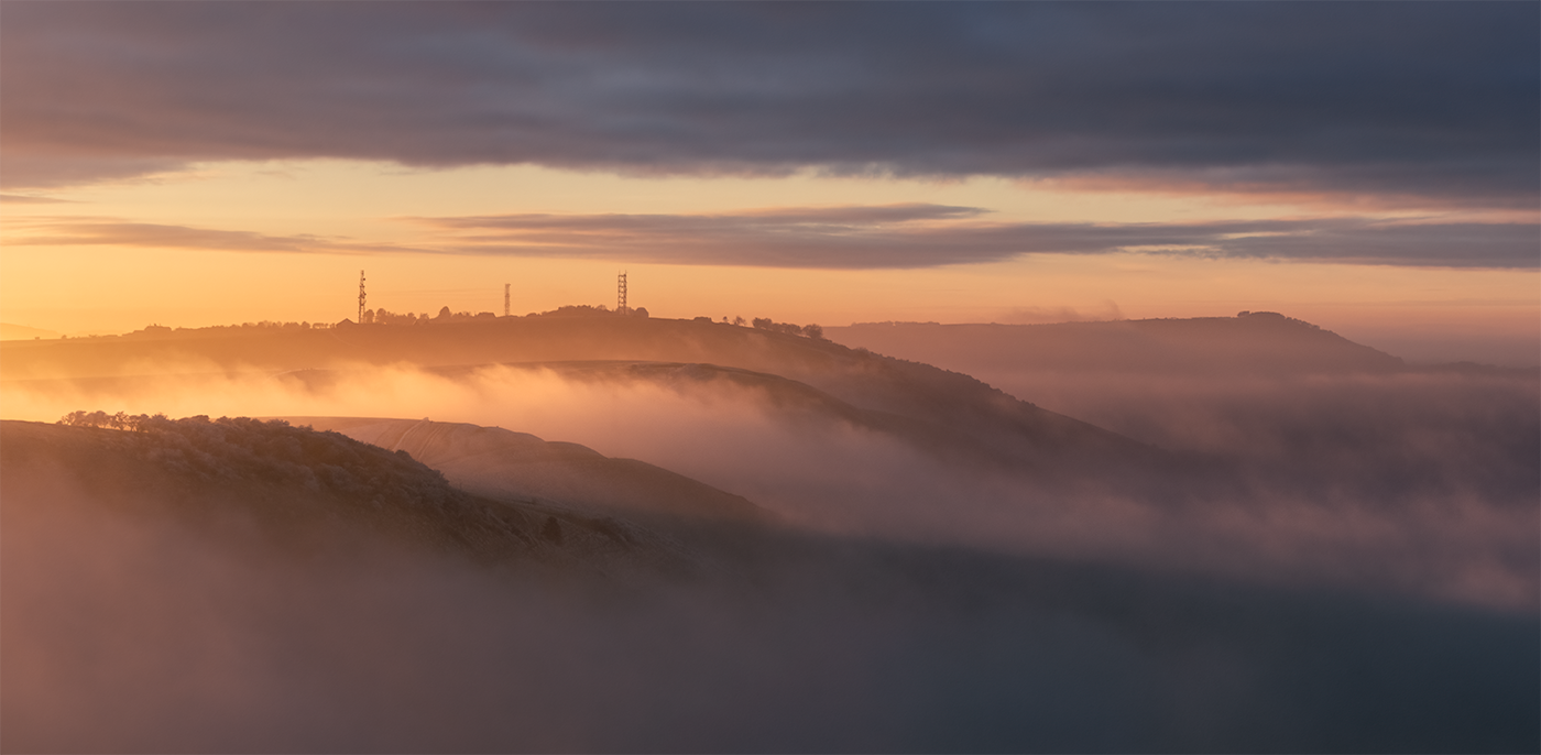 A bank of freezing fog flowing over the escarpments of the South Downs National Park during golden hour.