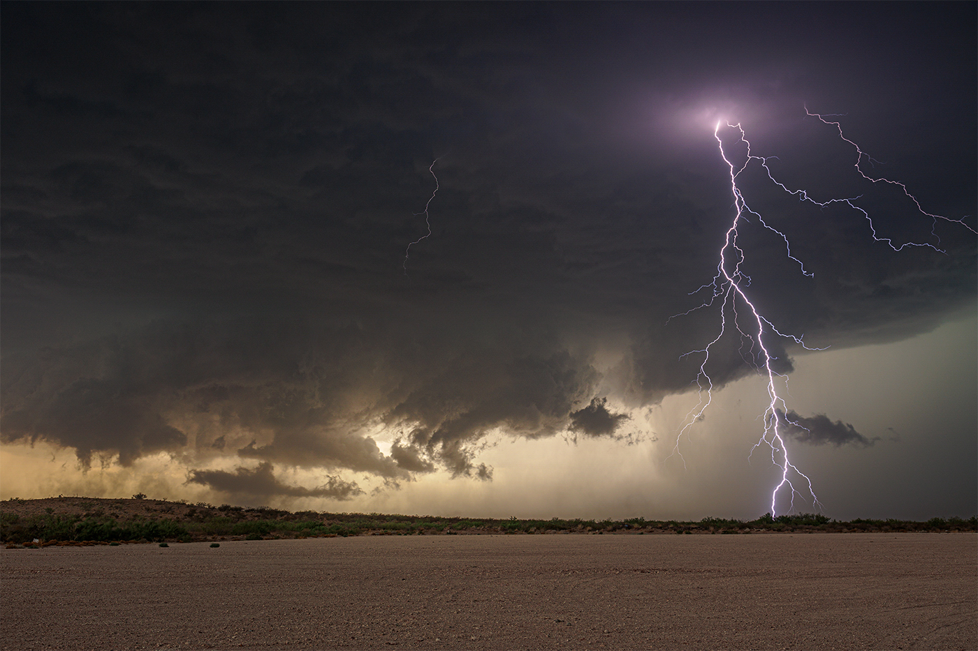 A savage forked lightning bolt striking the ground from the base of a supercell as a tornado develops against a sunset backdrop in New Mexico.