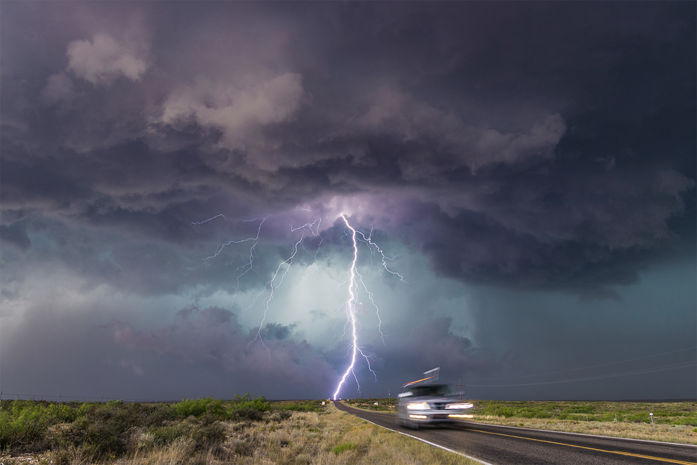 An impressive strong lightning bolt with many branches striking the end of the highway as a car drives away near Hagerman, New Mexico.