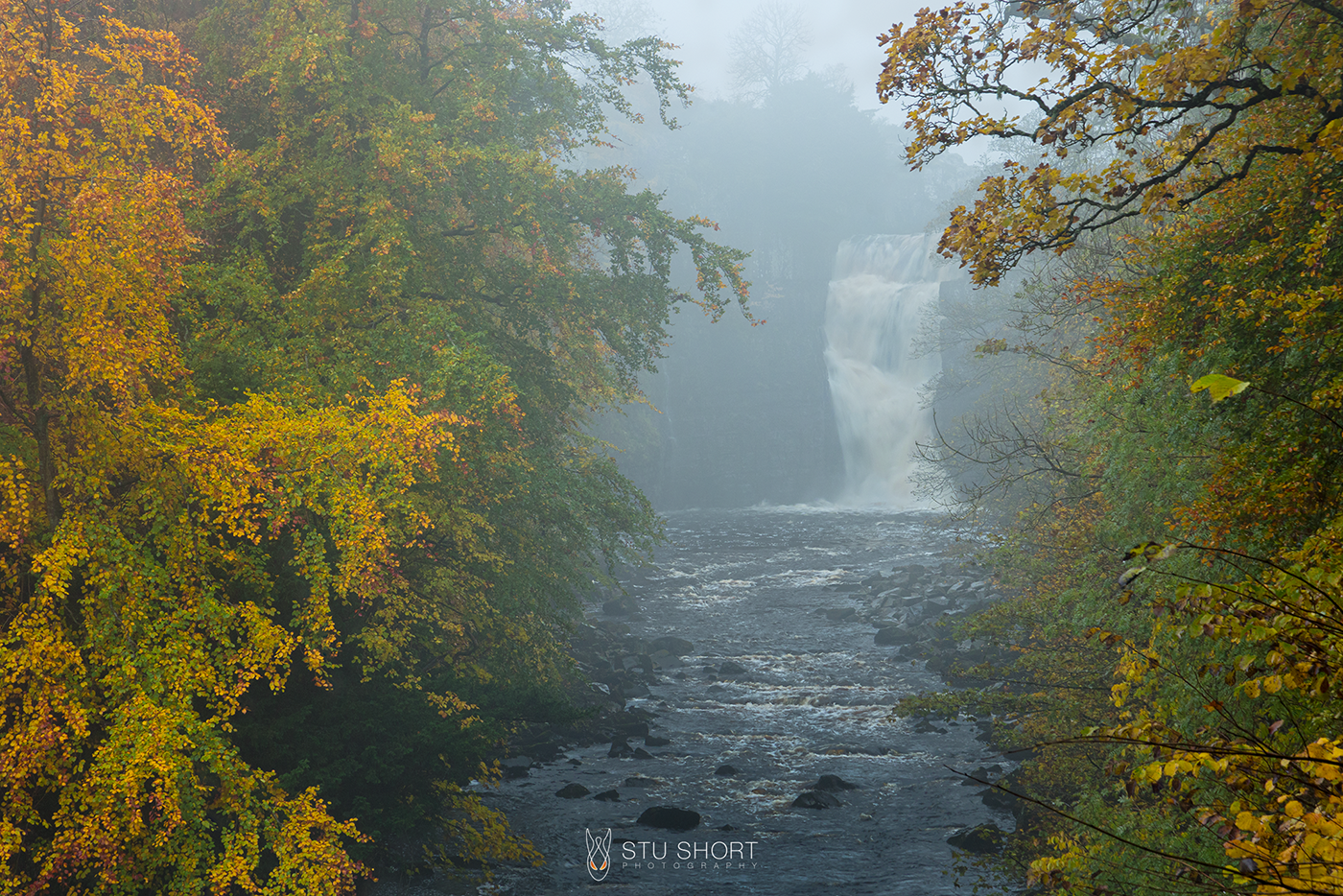 A serene river Tees flows gently, with a majestic waterfall cascading in the background, surrounded by lush autumn foliage.