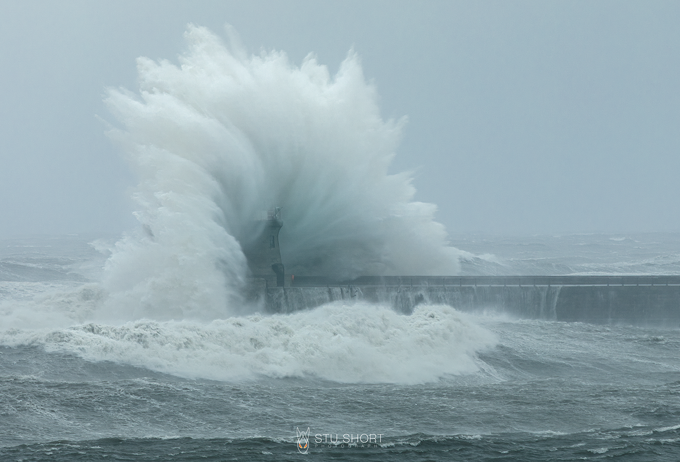 A powerful wave crashes dramatically over South SHields lighthouse, showcasing the force of nature against man-made structures