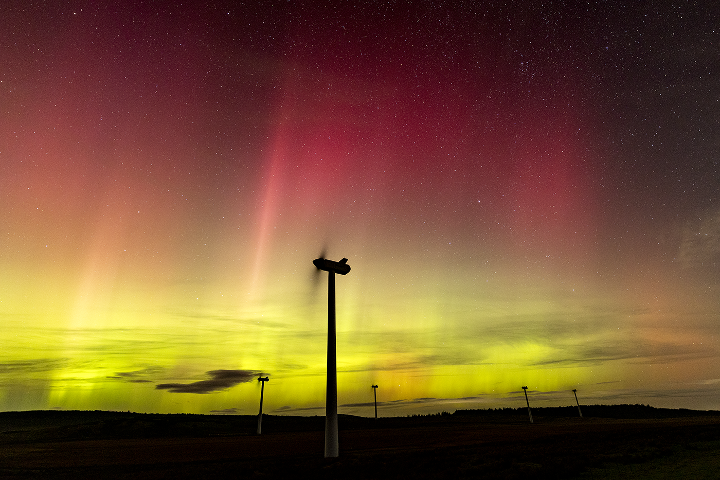 The aurora borealis illuminating the night sky above a row of wind turbines, creating a stunning natural spectacle.