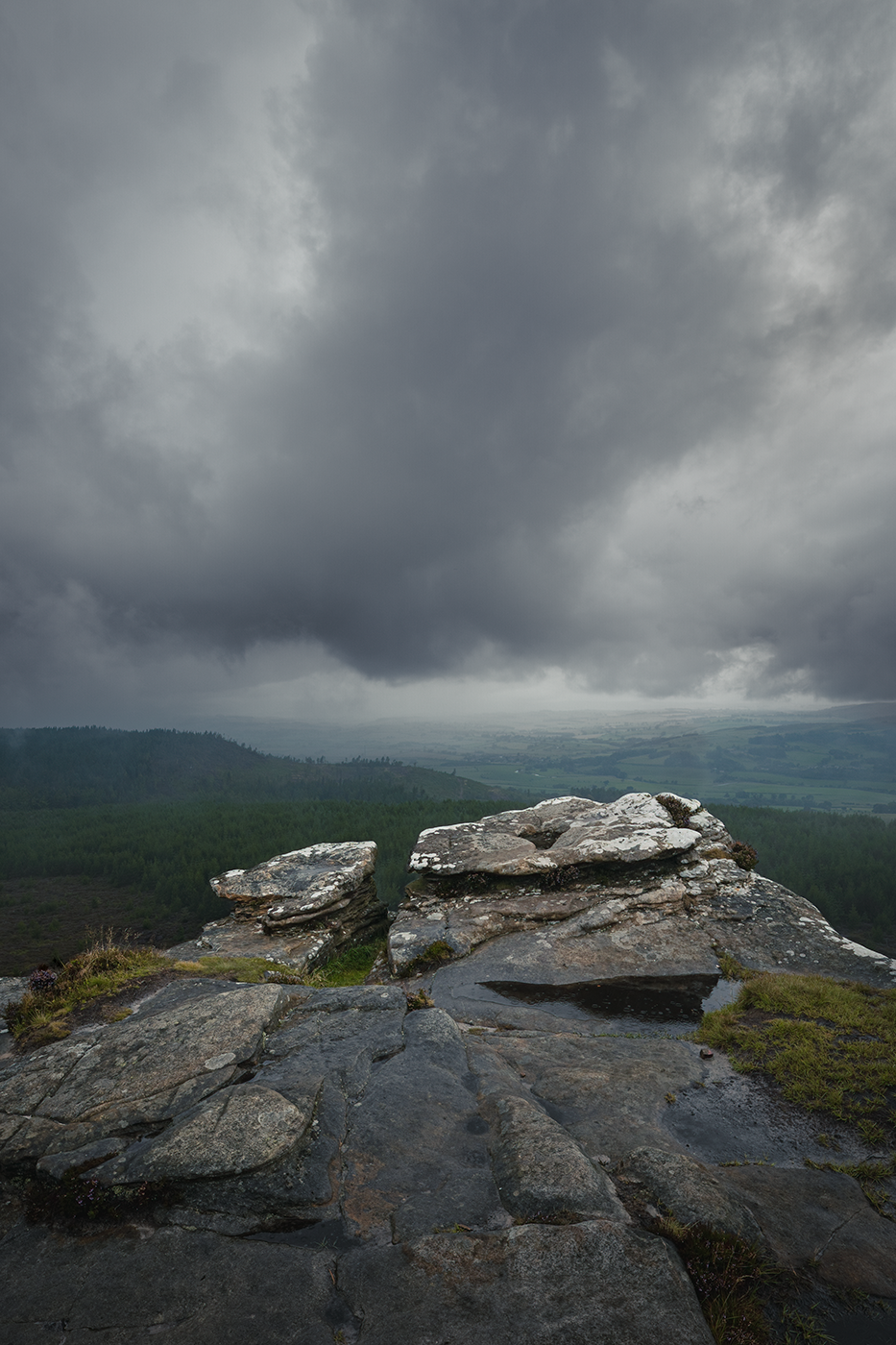 A rugged rocky outcrop overlooking a vast landscape backdrop as moody heavy clouds hang in the air.