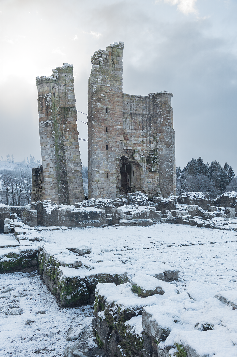 The majestic ruin of Edlingham Castle blanketed in snow, showcasing its grandeur against a wintery backdrop.