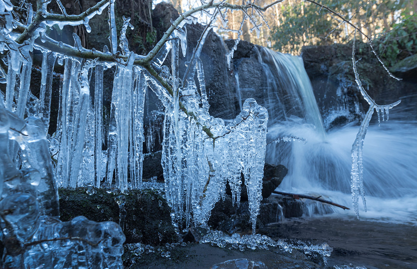 Winter landscape photography featuring a picturesque waterfall featuring hanging icicles, capturing the beauty of nature in a winter landscape.