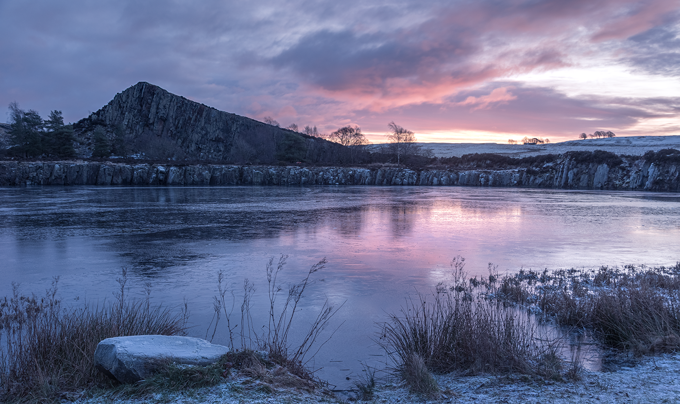 Winter landscape photography featuring a beautiful sunrise over the frozen lake of Cawfield Quarry as the escarpment towers in the background, showcasing nature's stunning colors and reflections.