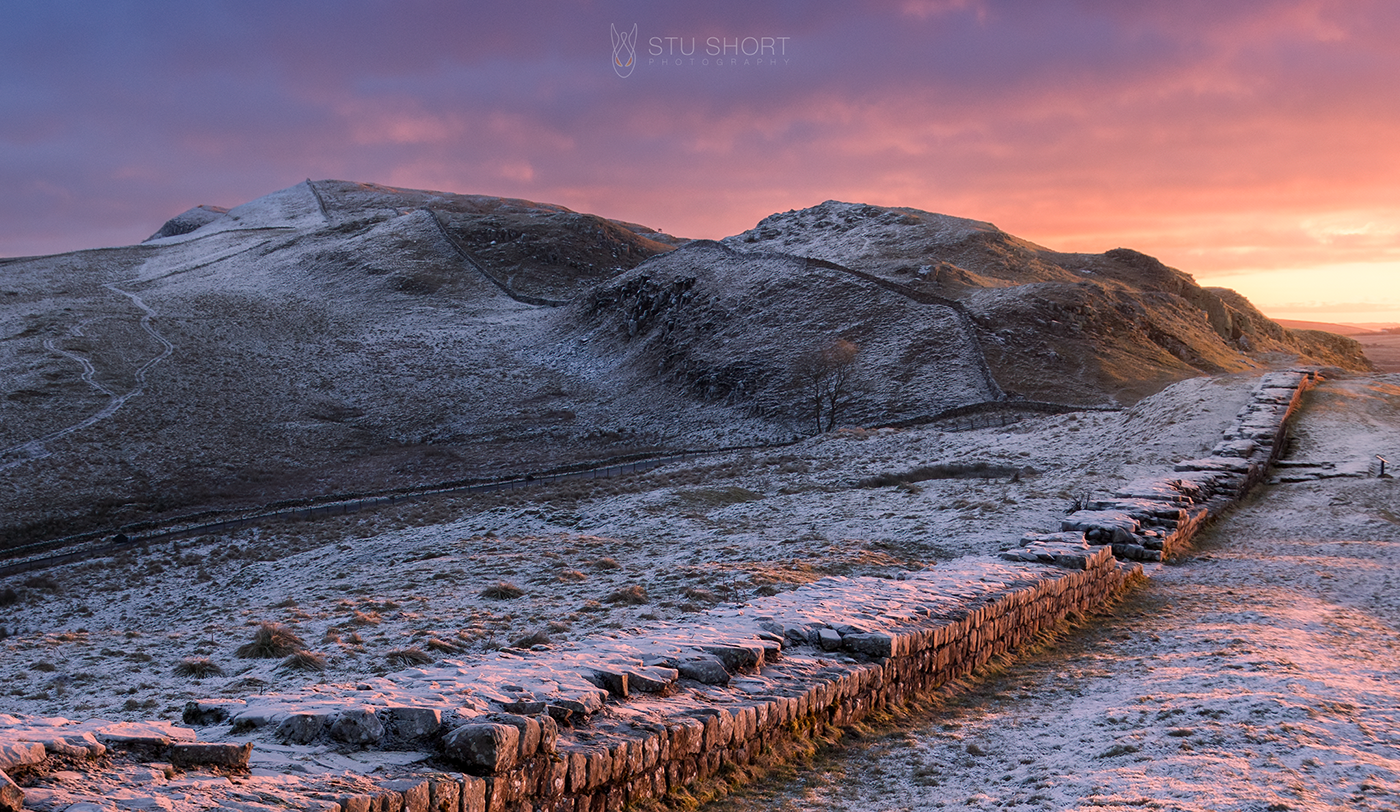 Winter landscape photography featuring a scenic view of a range of frost covered hills, featuring Hadrian's Wall that gracefully leads into the breathtaking landscape.