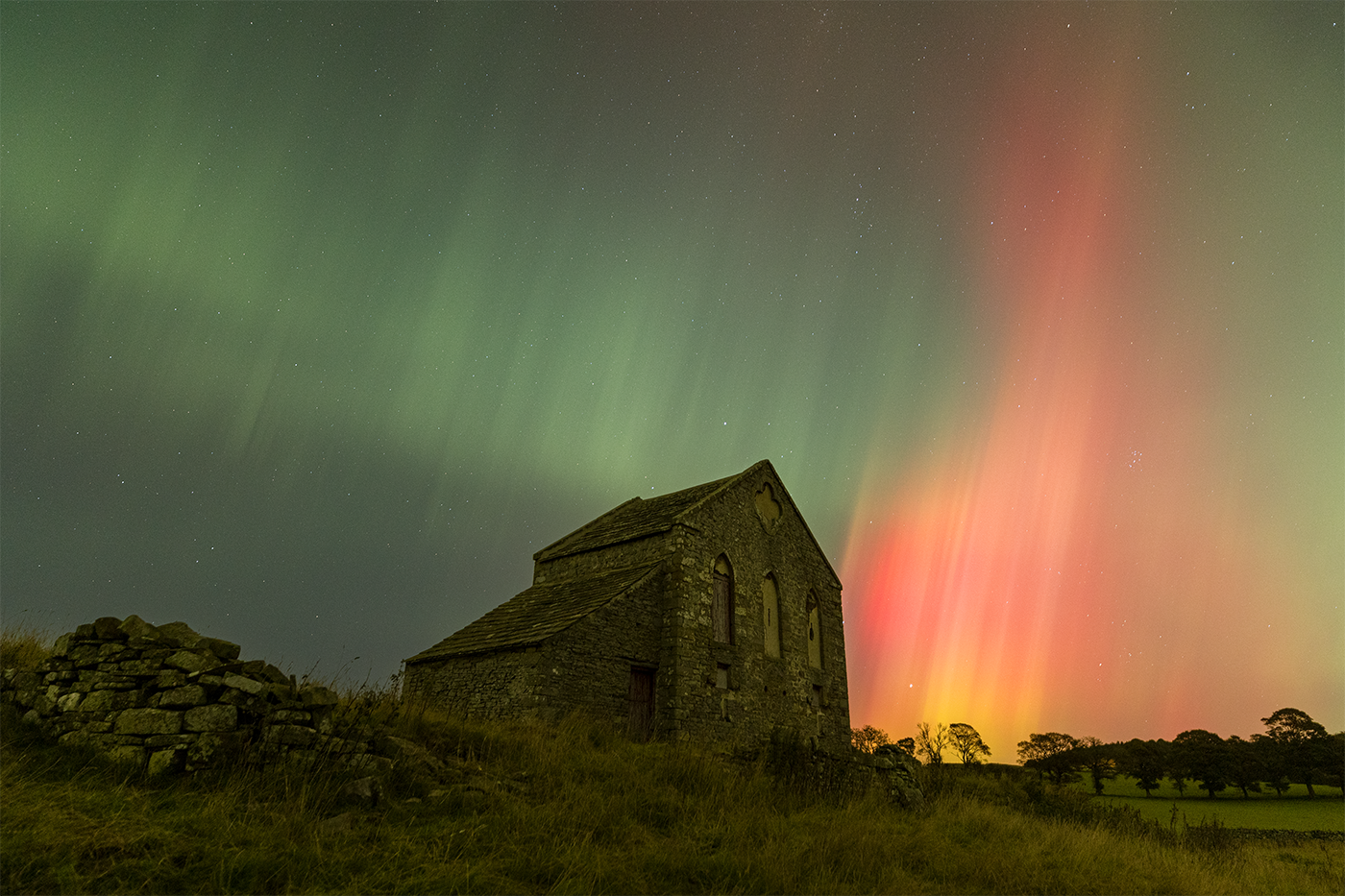 A tithe barn flanked by an enormous pillar of fire from a startling Northern Lights display.