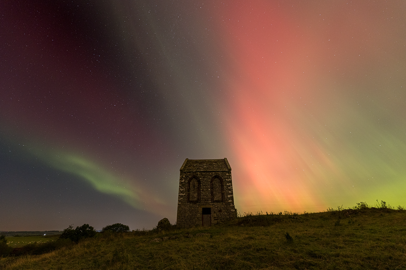 An 18th century tithe barn is silhouetted against an imposing display of the Northern Lights.