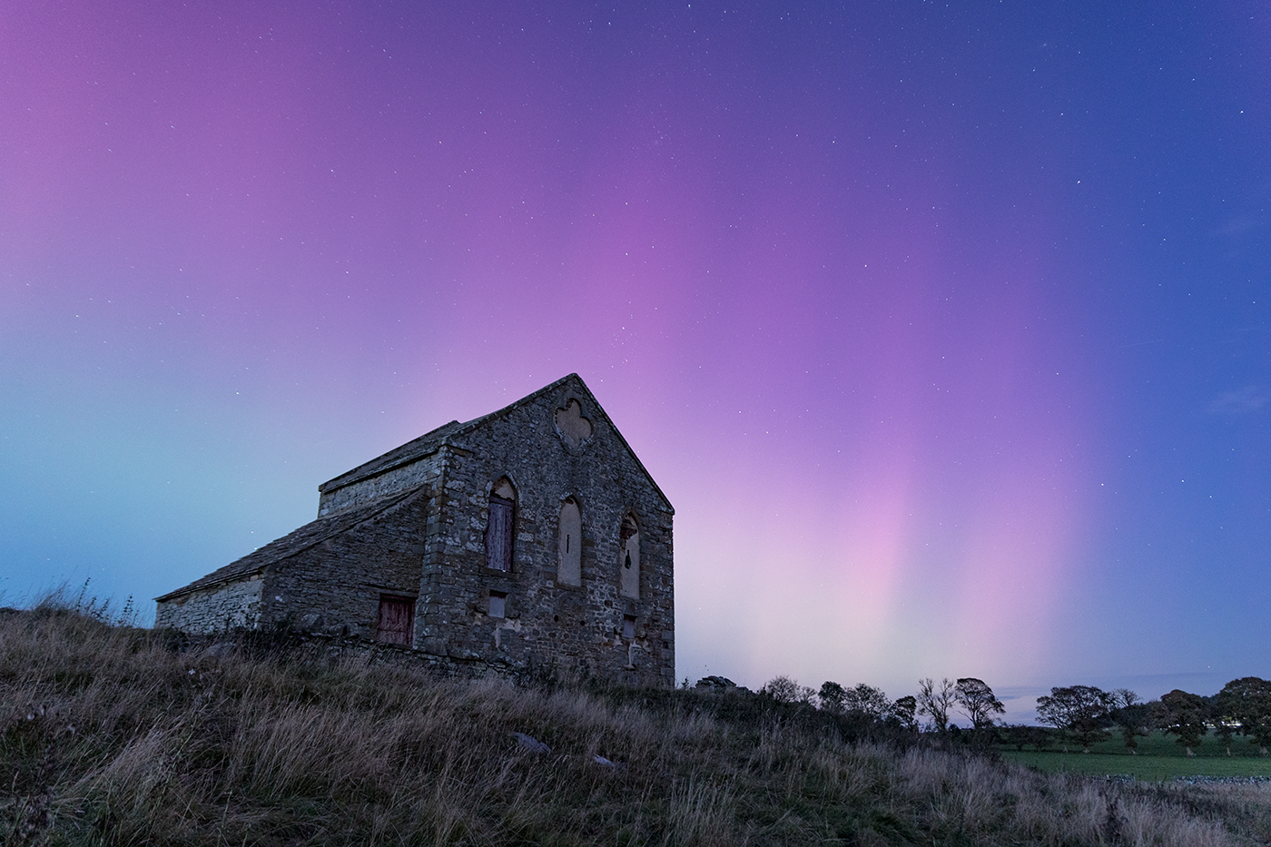 Magenta pillars from an aurora display start to become visible through the twilight.