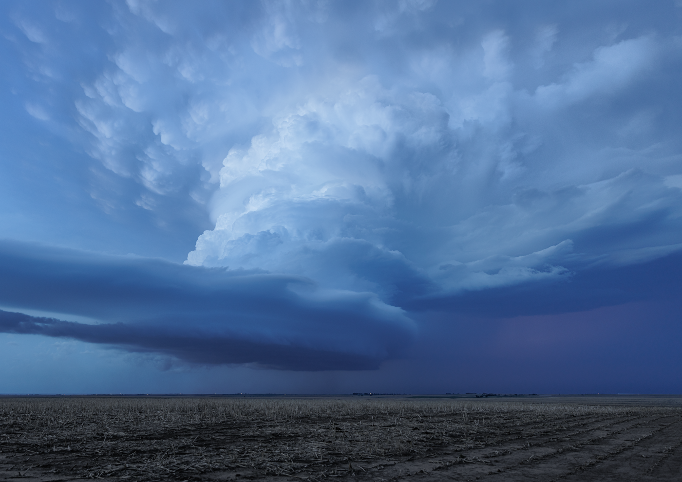 Large, anvil-shaped cumulonimbus cloud formation over a barren field, indicating a severe thunderstorm.