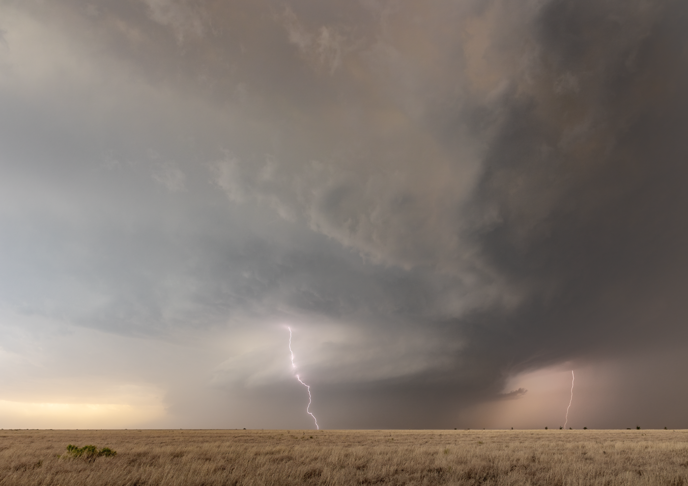 Massive supercell storm with lightning bolts striking the ground in a desert landscape.