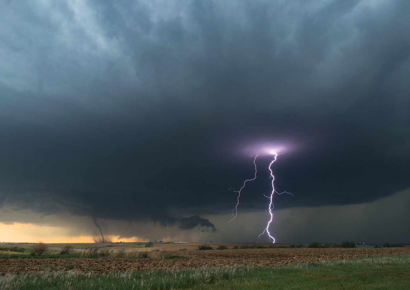 Large tornado touching down with lightning strikes illuminating a stormy sky.