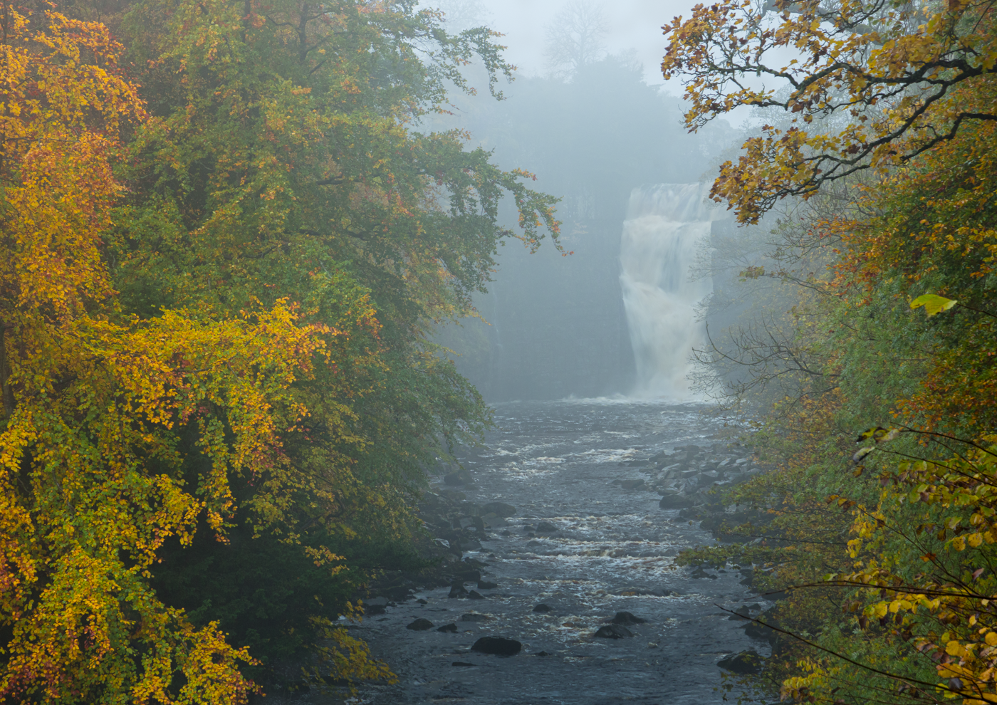 Misty waterfall in an autumn forest with colorful foliage surrounding it.