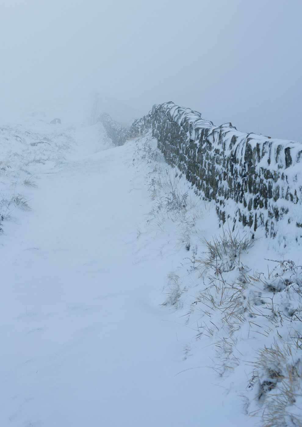 Snowy path alongside a stone wall disappearing into the mist.