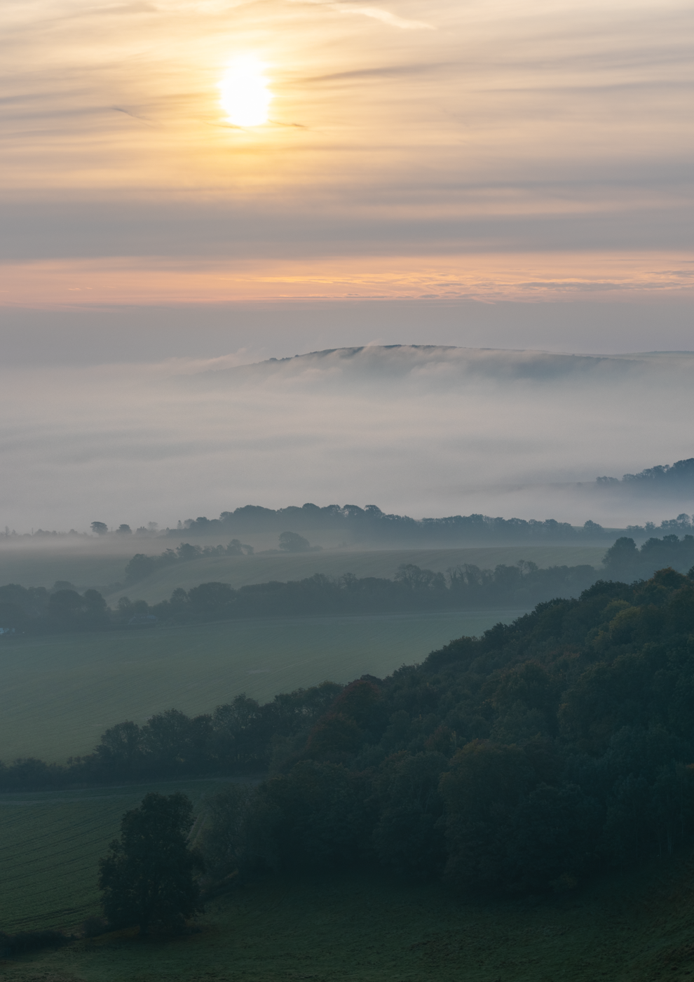 Misty valley landscape with rolling hills and soft sunlight.