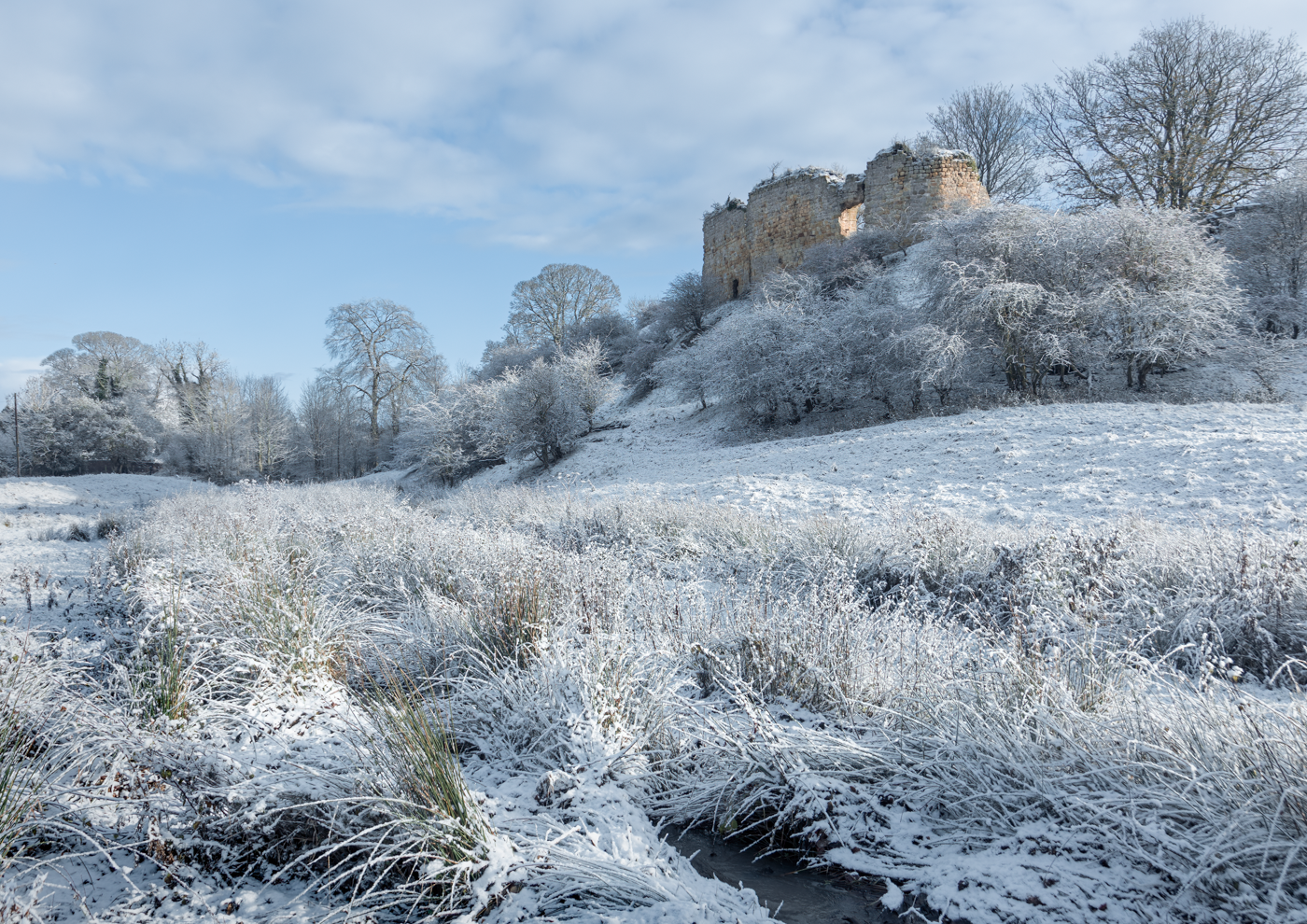 Snow-covered ruins of Mitford Castle in a winter landscape.