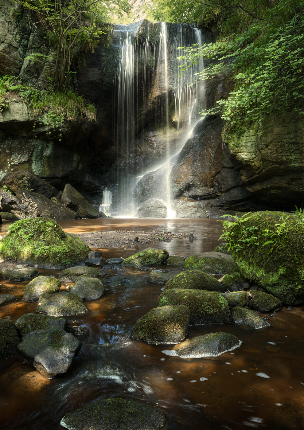 Peaceful waterfall flowing over mossy rocks in a sunlit setting.