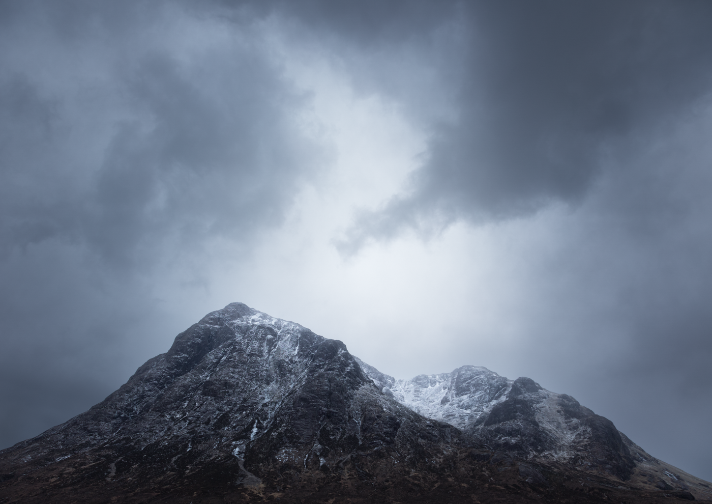 Snow-capped mountain peak with dramatic clouds overhead.