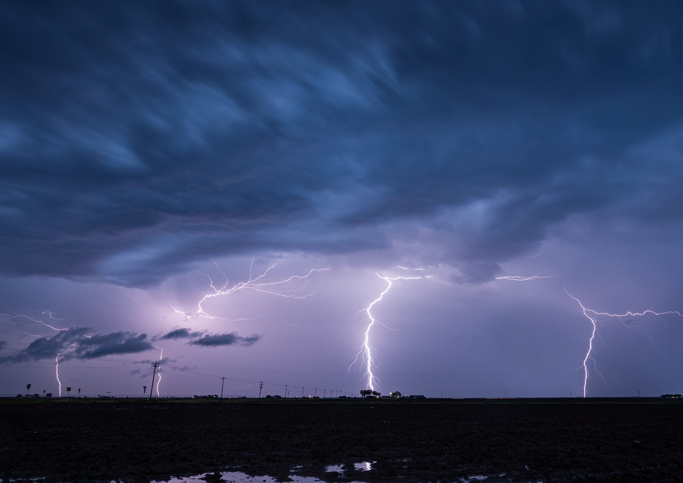 Intense lightning storm with multiple strikes illuminating a dark sky over a field.